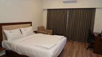Een hotelkamer met een bed, een stoel, een bureau en een airconditioning.