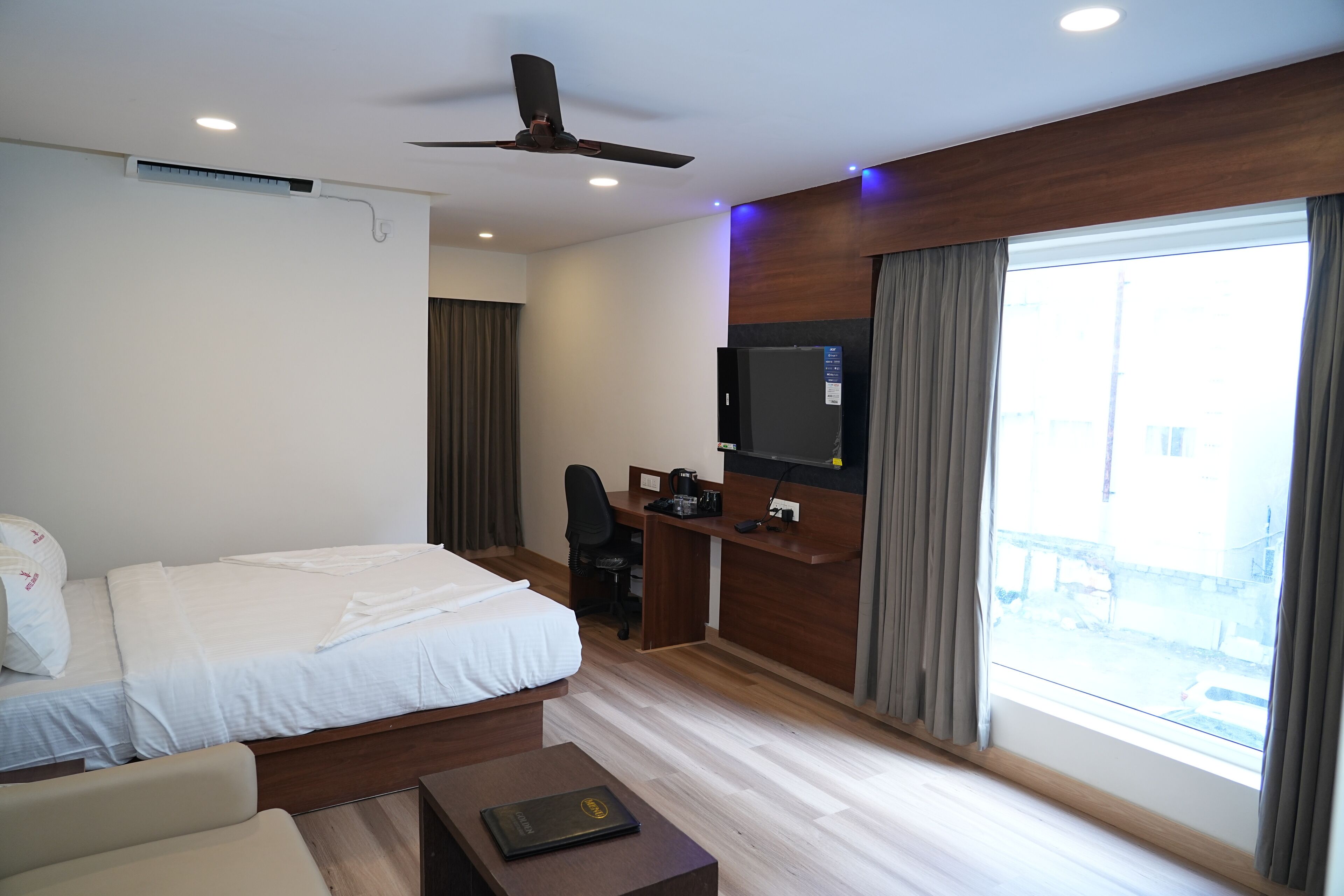 Une chambre d’hôtel avec un lit, un bureau, une télévision et une fenêtre avec des rideaux.