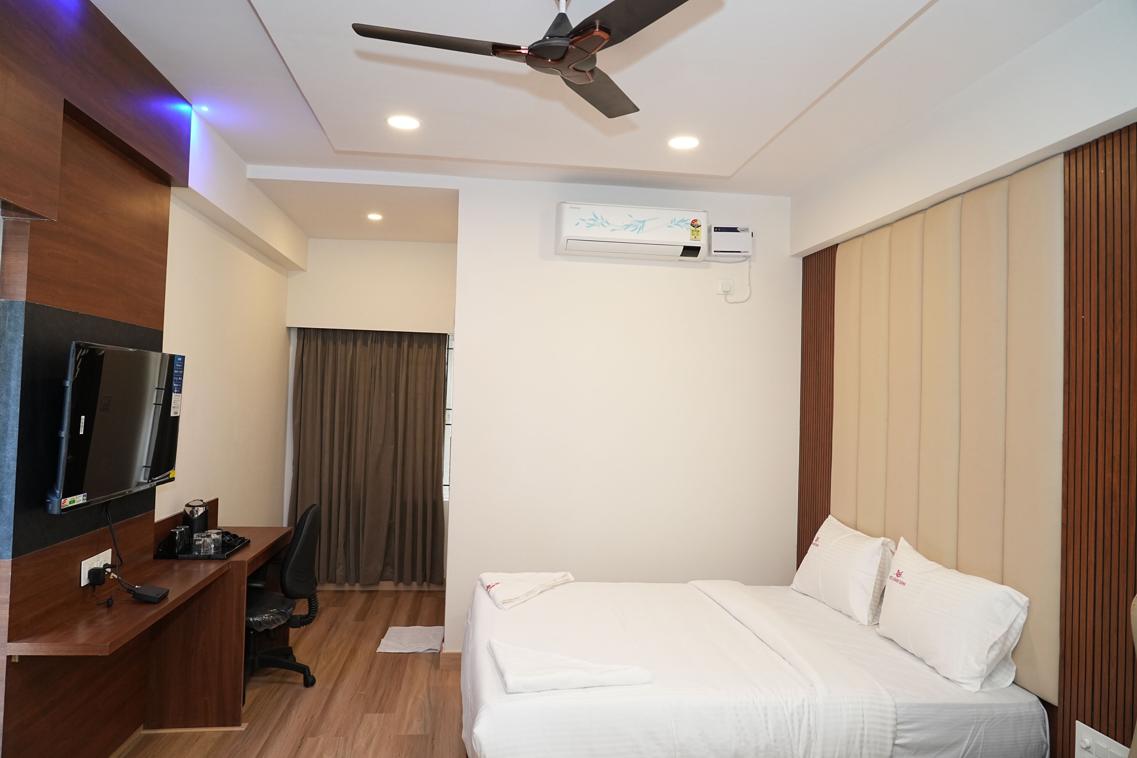 A hotel room with a bed, a desk, a television, and an air conditioning unit.