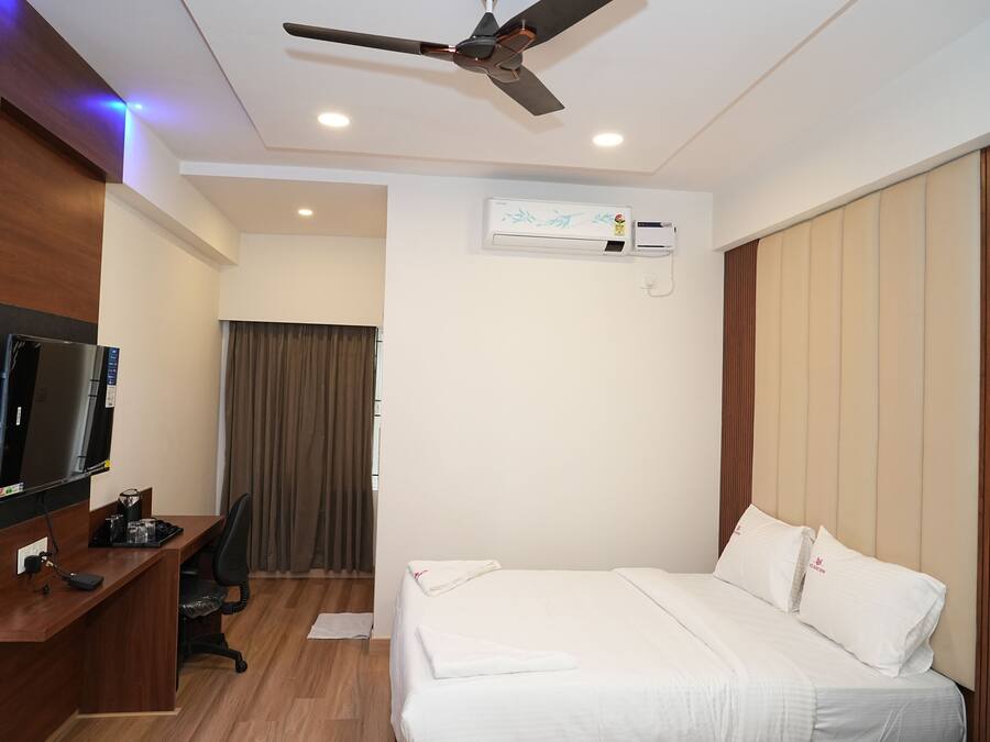 A hotel room with a bed, a desk, a television, and an air conditioning unit.