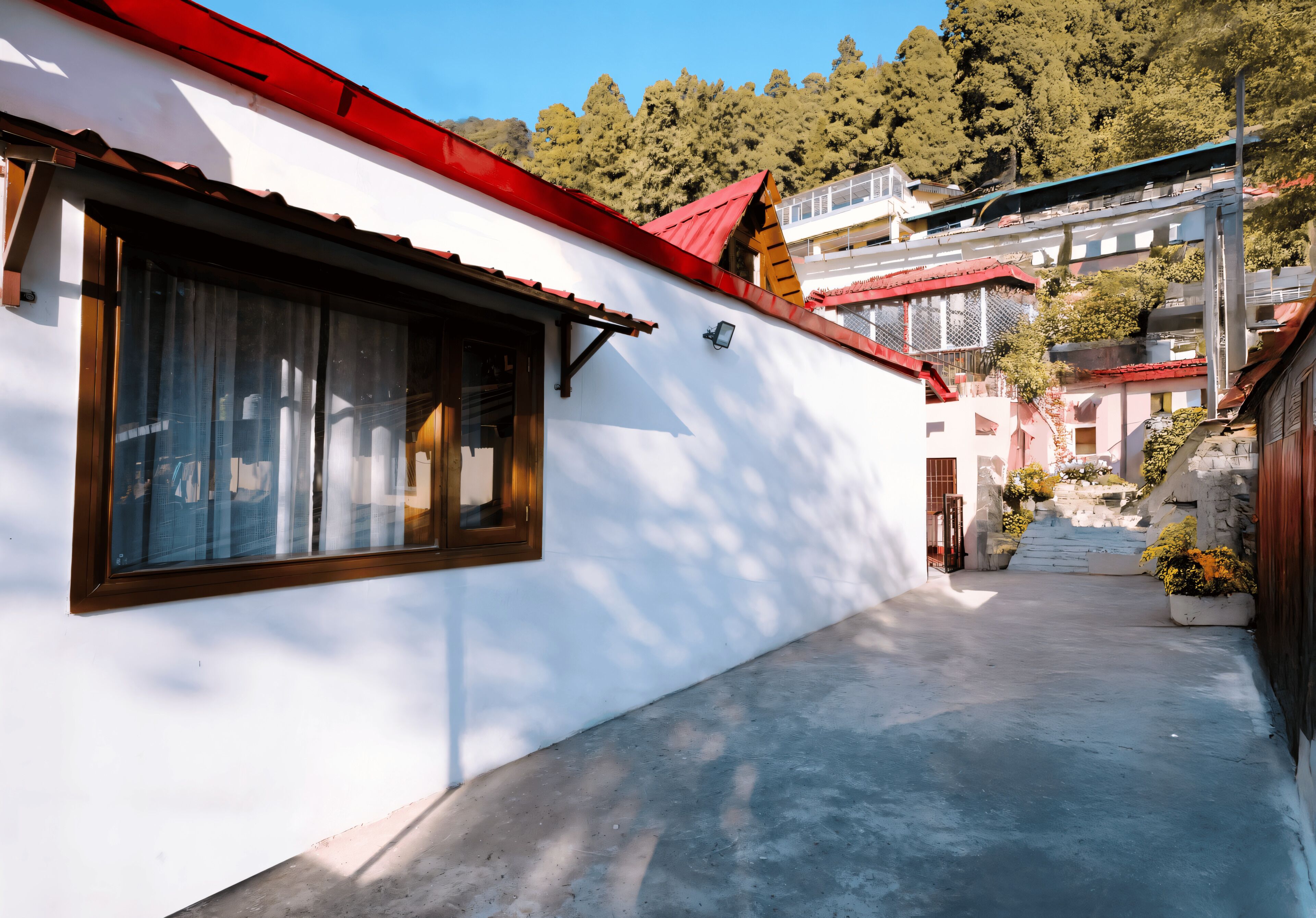 A narrow alleyway with a white building on the left, a red roof, and a staircase leading up to a building with a blue roof.