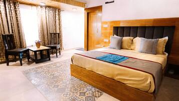 A hotel room with a large bed, a wooden headboard, a small table with chairs, and a patterned rug.