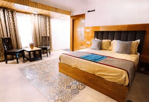 A hotel room with a large bed, a wooden headboard, a small table with chairs, and a patterned rug.