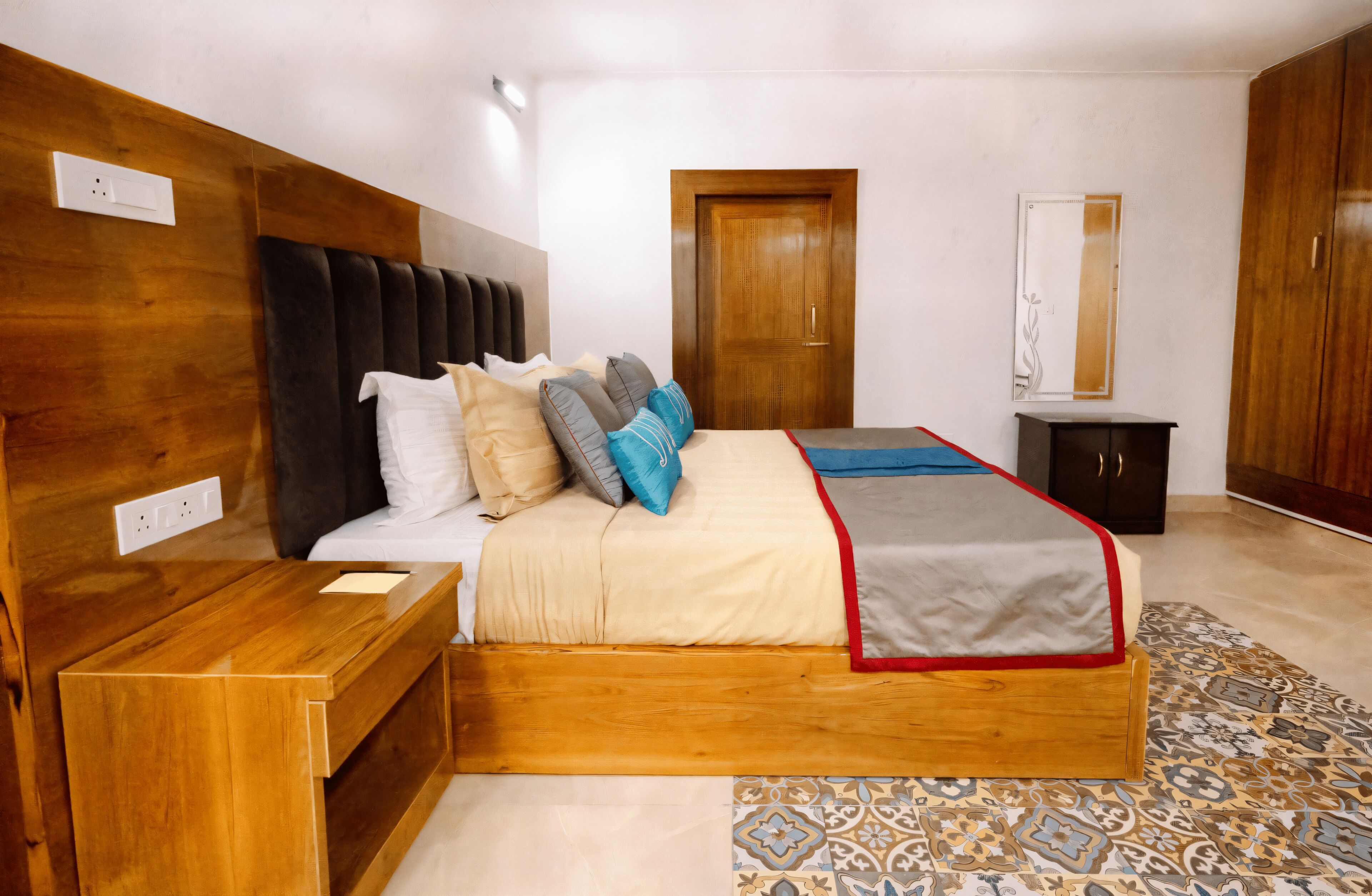 A bedroom with a wooden headboard, a bed with multiple pillows, a bedside table, a wardrobe, and a patterned rug.