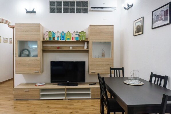A modern living room with a flat-screen TV, wooden cabinets, and a dining table with chairs. - Spacious apartment within walking distance of the historic center and shopping streets (Cagliari)
