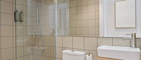 Un baño moderno con ducha de vidrio, inodoro y lavamanos con encimera de madera.