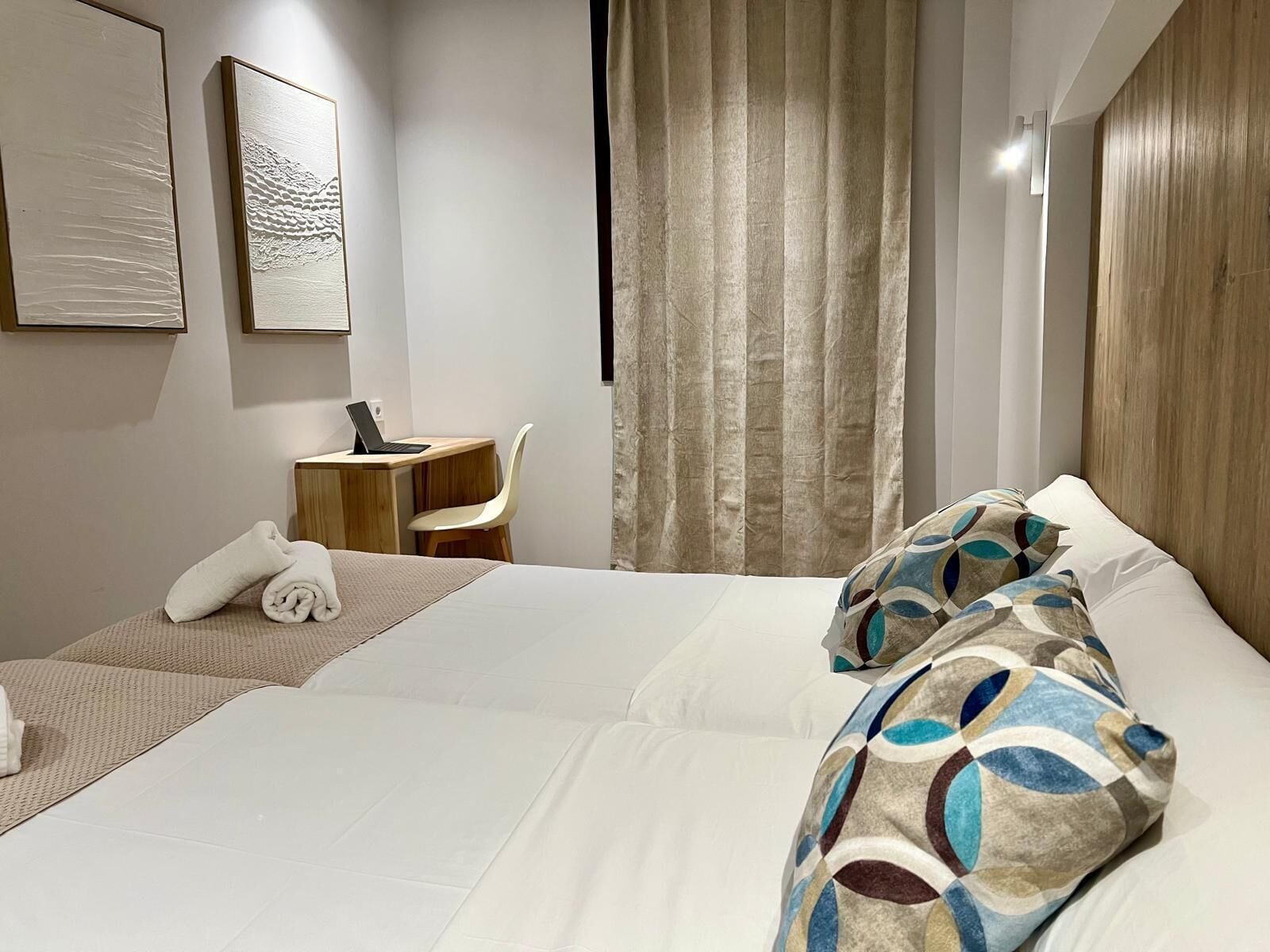 A hotel room with a bed, a desk, a chair, and a curtain.