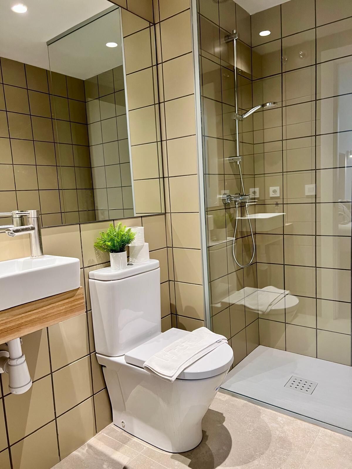 Un baño moderno con cabina de ducha de vidrio, inodoro blanco y lavamanos con espejo.