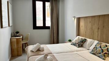 Habitación de hotel moderna con dos camas, un escritorio con una computadora portátil, una silla y una ventana con cortinas.