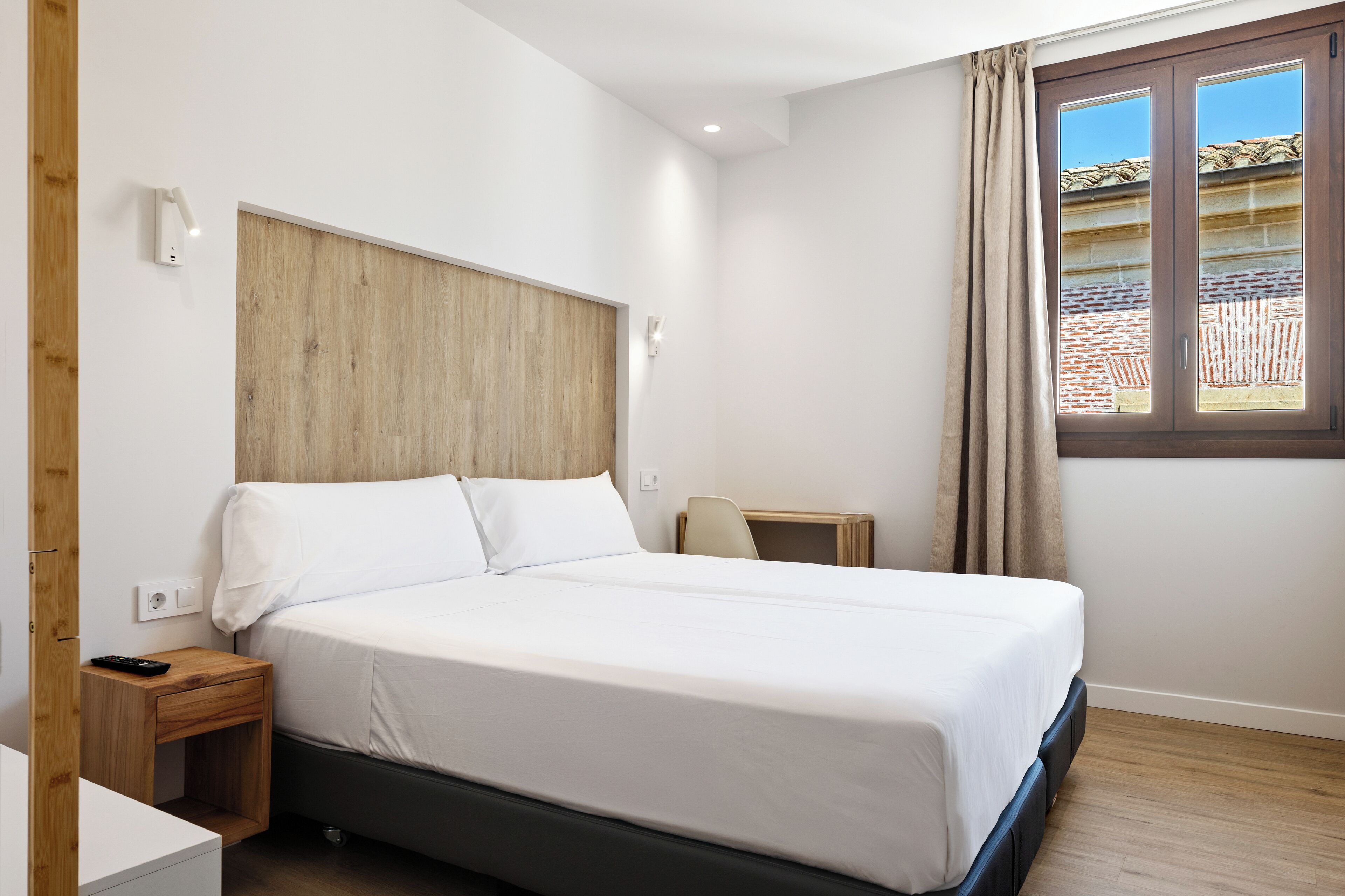 Un dormitorio con cama, mesita de noche y ventana con cortinas.