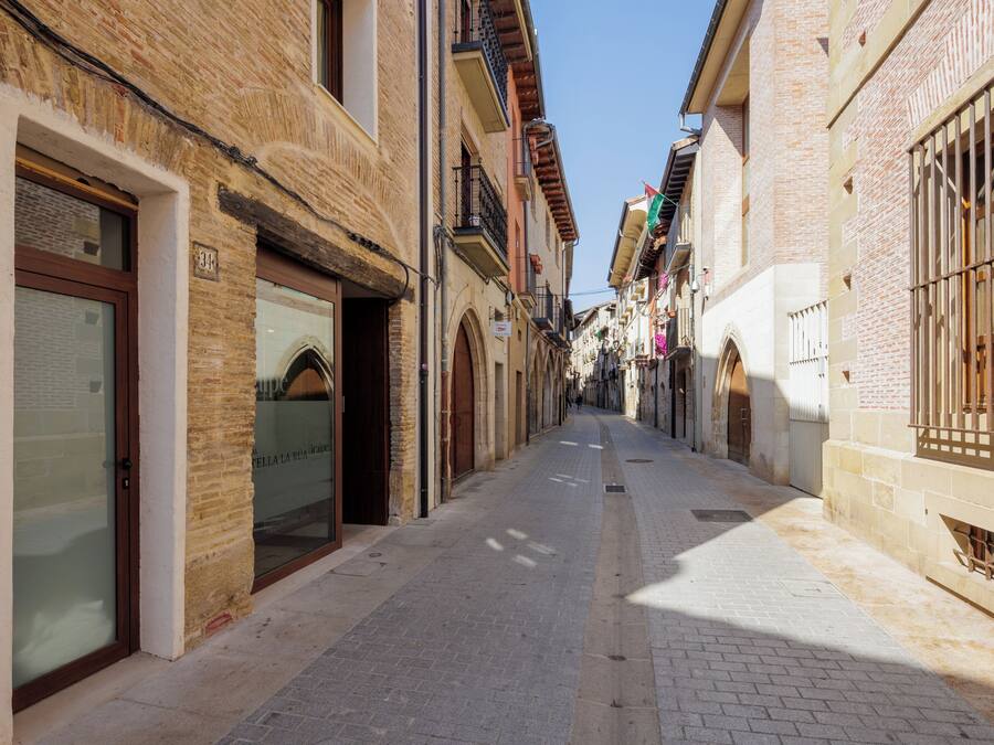 Eine enge Straße gesäumt von traditionellen Gebäuden mit Rundbögen und Fenstern, darüber ein klarer Himmel.