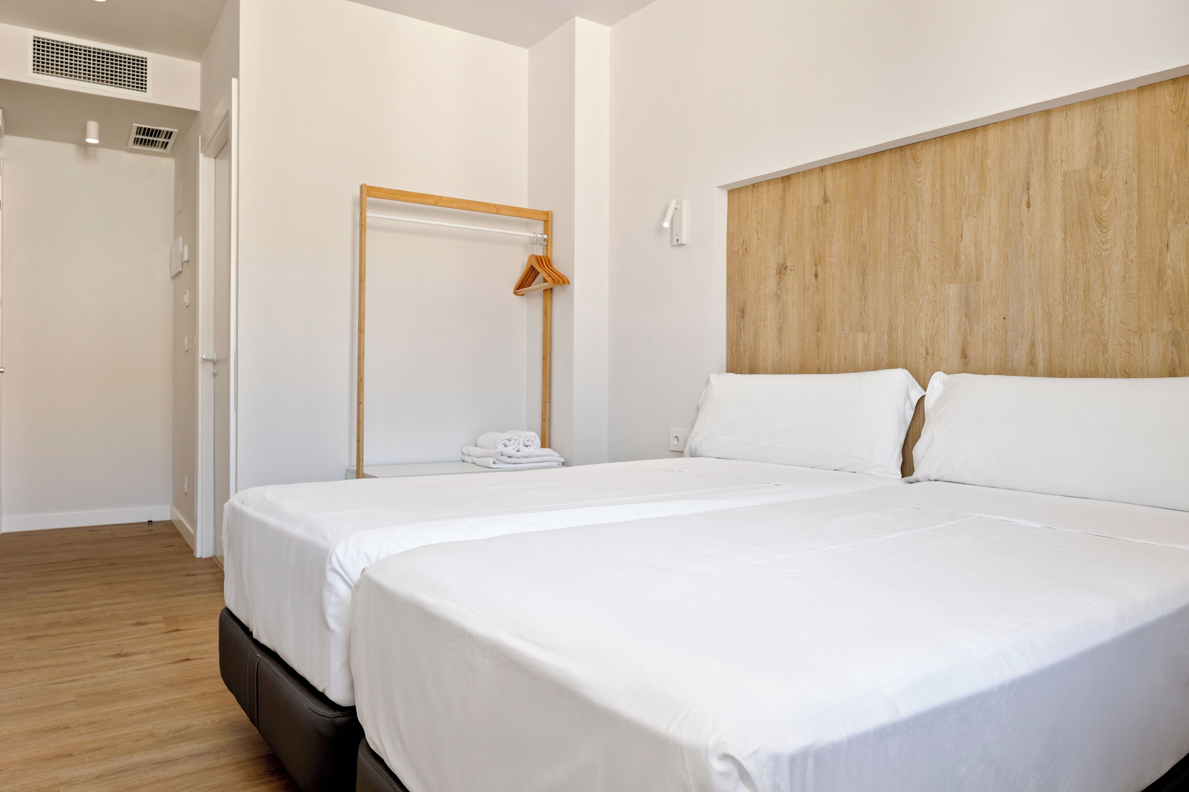 A hotel room with a large bed, a wooden headboard, a door with a coat hanger, and a white wall.