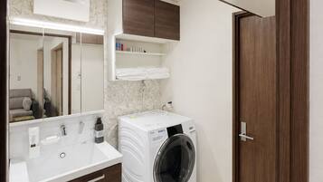 A modern bathroom with a built-in washing machine, a large mirror, and a wooden door.