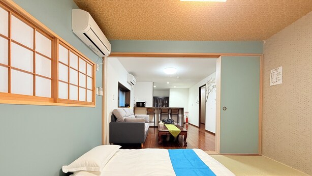 Una habitación con cama, sofá, una mesa de comedor con sillas y una cocina al fondo.