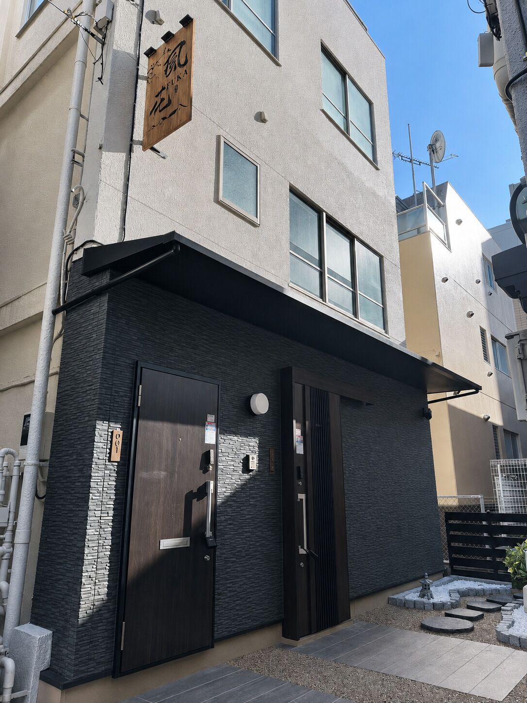 A modern building with a flat roof, a wooden sign with Japanese characters, and a door with a keypad lock.