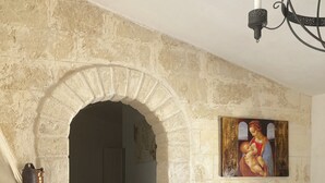 A room with a stone archway leading to a kitchen, a television on a wooden cabinet, and a painting above the archway. - Villa Sara of Apulia - Triple (Masseria Gaudella)