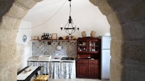 A rustic kitchen with a stone archway, a gas stove, wooden cabinets, and a hanging chandelier. - Villa Sara of Apulia - Triple (Masseria Gaudella)