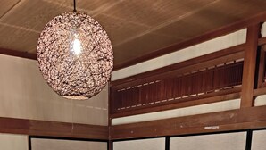 Un salon moderne avec un canapé d’angle, un luminaire suspendu, des tatamis et des portes coulissantes traditionnelles.