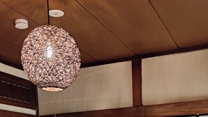 Une pièce de style japonais traditionnel, avec un sol recouvert de tatamis, une petite table en bois, des portes coulissantes en papier de riz (shoji) et un luminaire suspendu.