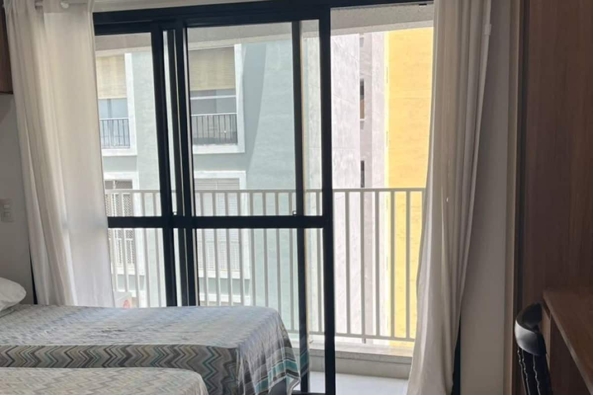 A hotel room with a bed, a desk, a chair, and a balcony with curtains.