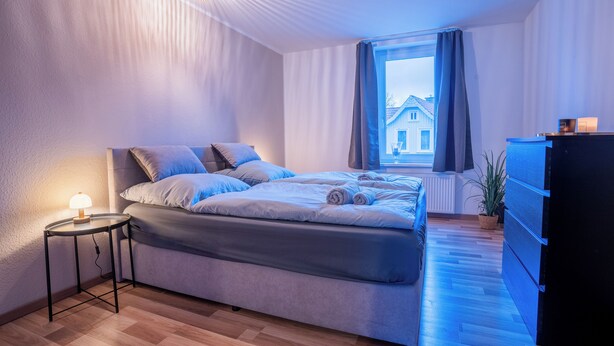 Une chambre à coucher moderne avec un lit, une table de chevet et une fenêtre avec des rideaux.