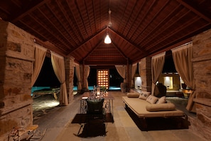 A cozy, rustic room with a stone wall, a wooden ceiling, a sofa, a table, and a chair.