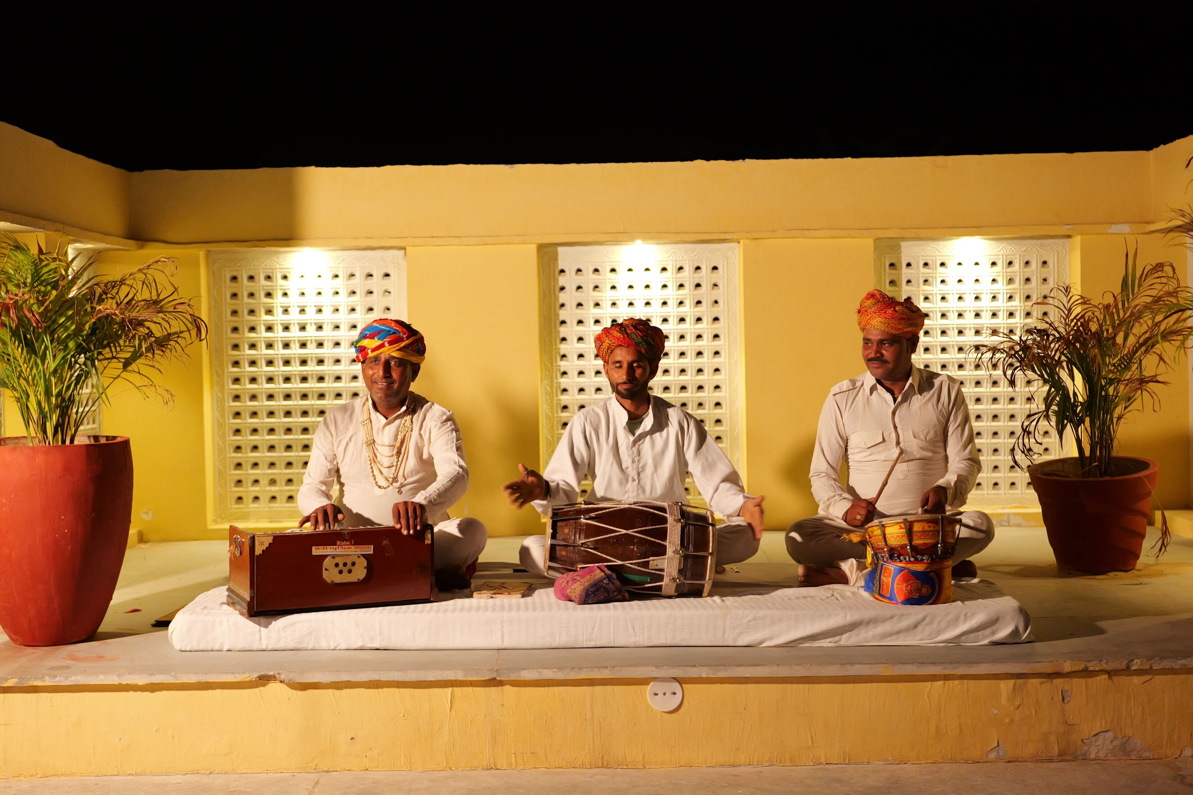 Three individuals seated on a bench outdoors at night, playing traditional drums.
