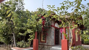 A stone pathway leading to a red and white building with a wooden door and steps. - Neem Sarai Sariska (Rajgarh)
