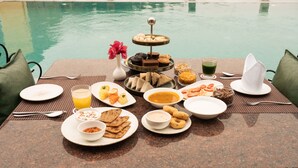 A breakfast buffet with various dishes and drinks by a poolside table. - Neem Sarai Sariska (Rajgarh)