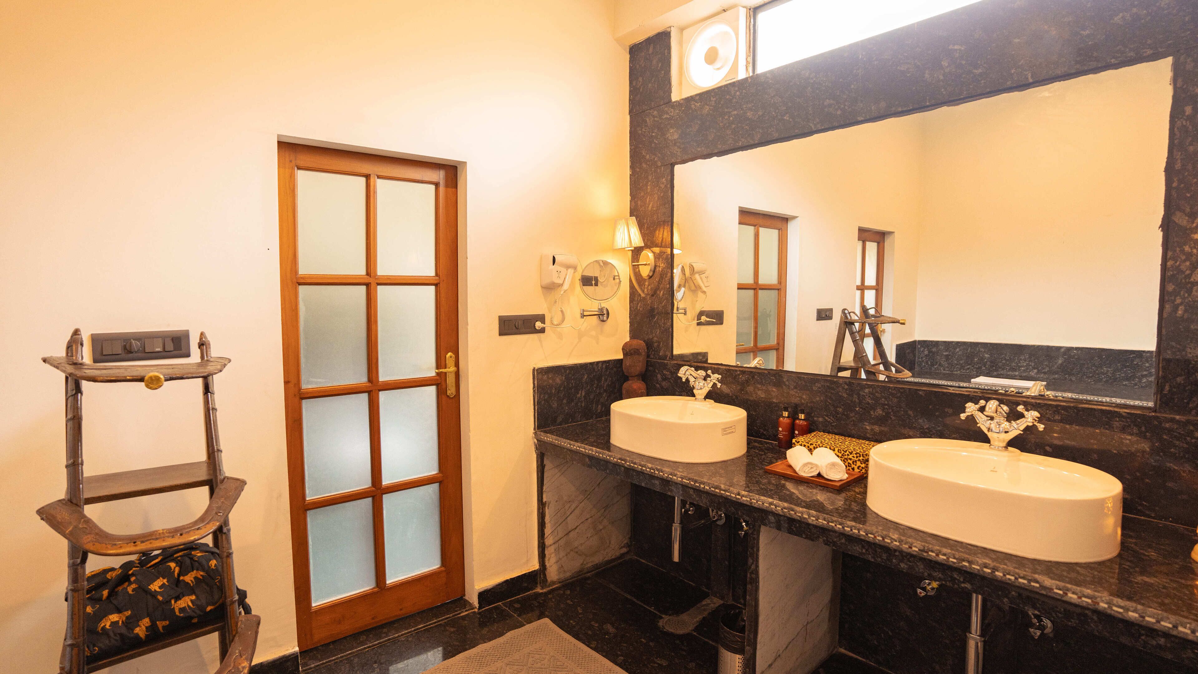 A bathroom with two sinks, a large mirror, and a wooden door with frosted glass panels.