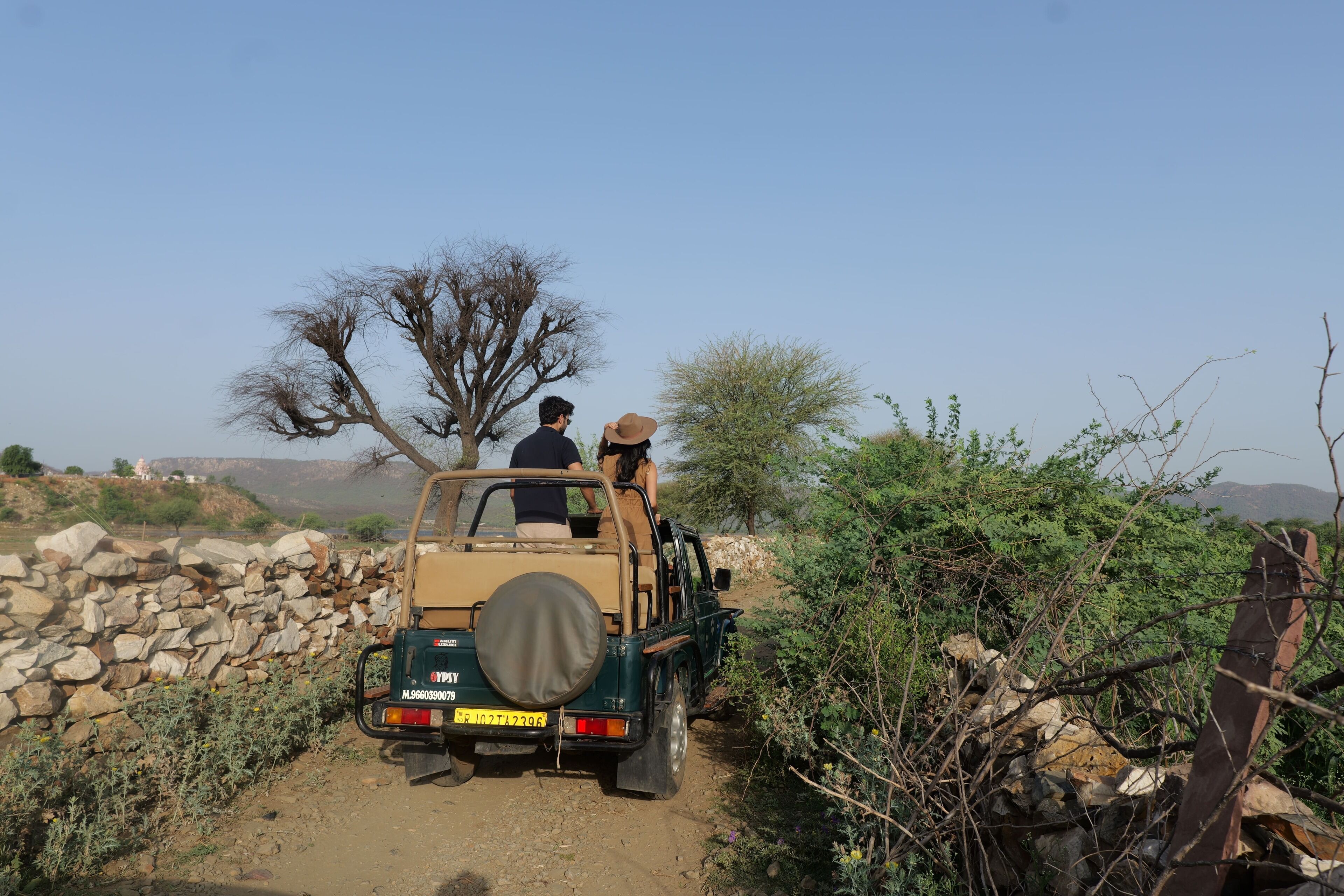 Un véhicule de safari est garé sur un chemin de terre, avec un mur rocheux d’un côté et une végétation clairsemée de l’autre.