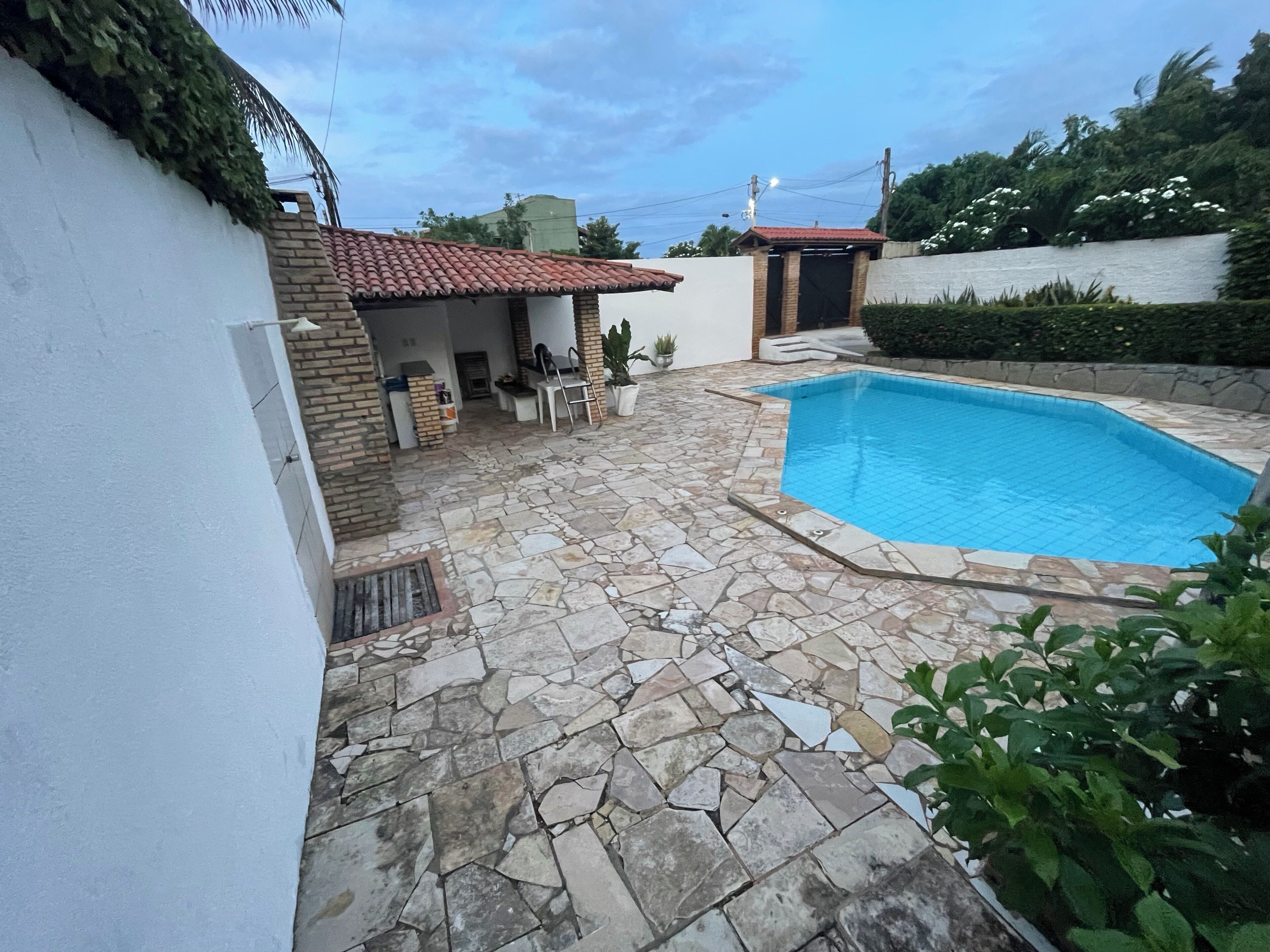 A swimming pool with stone tiles, a white wall, and a brick building with a tiled roof.