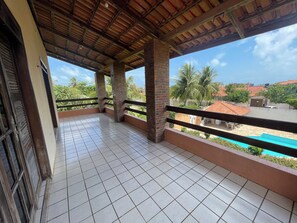 A covered balcony with tiled flooring, brick pillars, and a view of a swimming pool and palm trees.