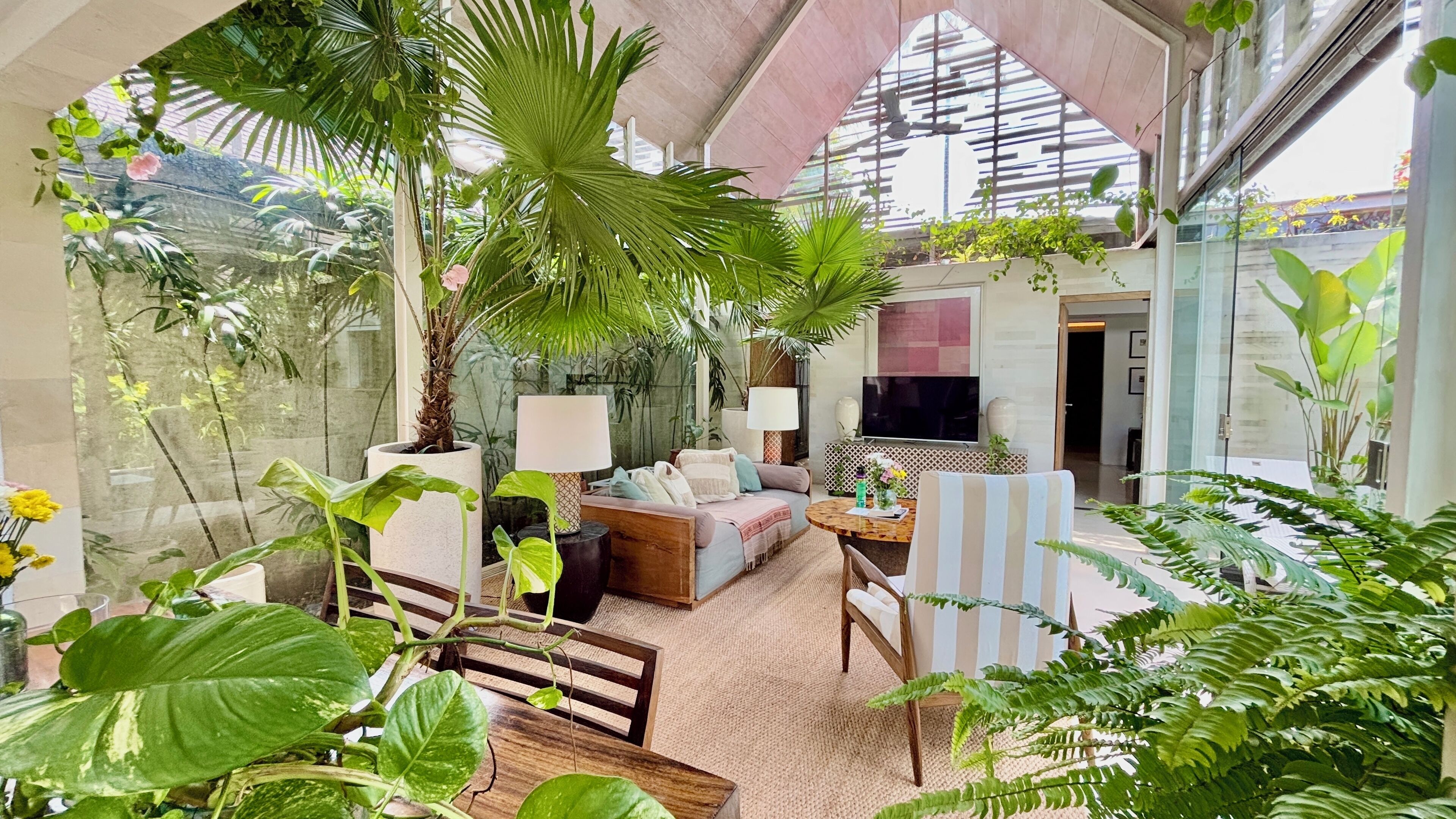 Ein modernes Wohnzimmer mit einer Couch, einem Couchtisch und Sesseln, umgeben von üppigen Grünpflanzen und einem großen Panoramafenster.