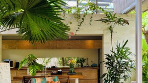 A modern kitchen with wooden cabinets, a dining area with a round table, and a large potted plant. - Kawung Villa Canggu (Canggu)