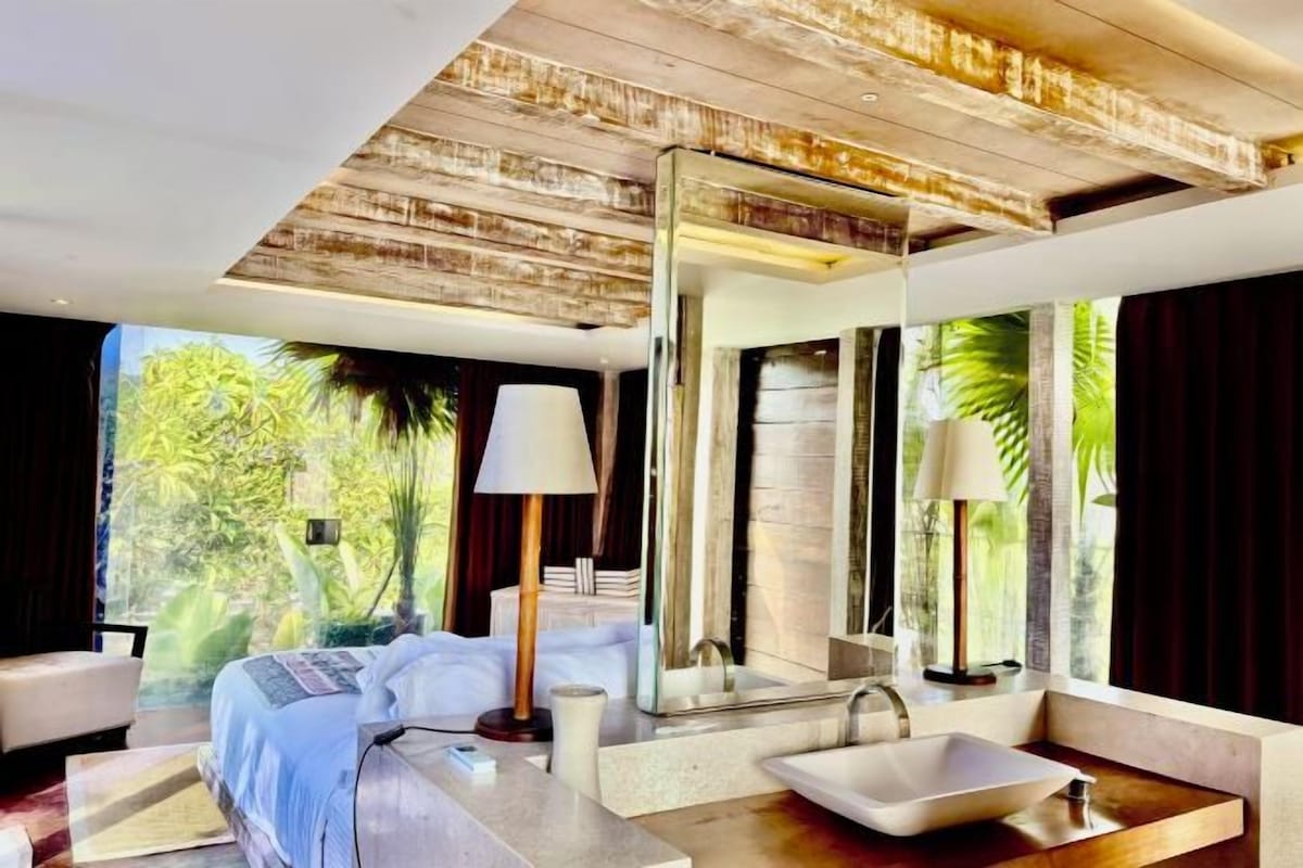 Un dormitorio moderno con una cama grande, un baño con un espejo amplio y vistas a zonas verdes.