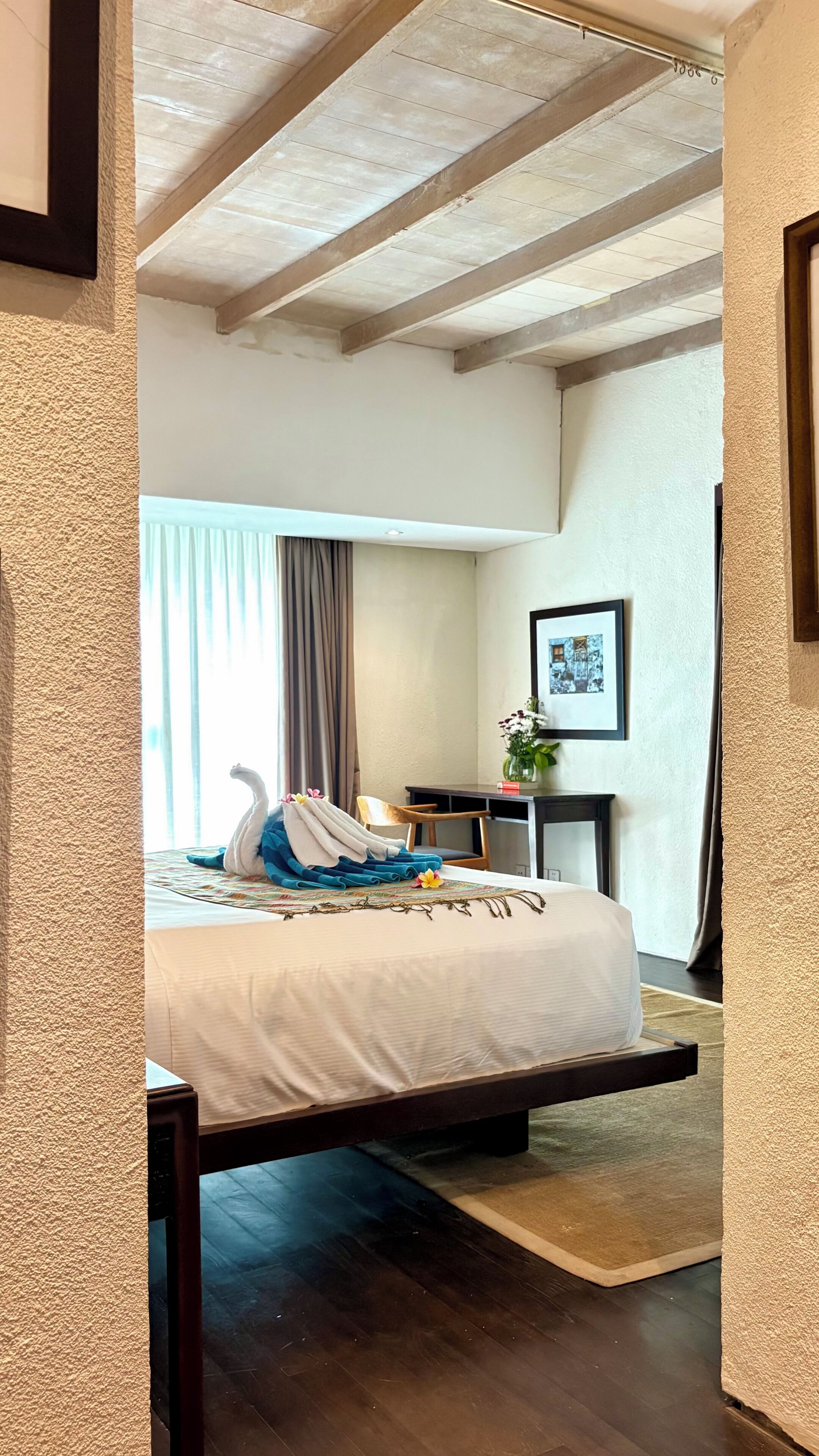 Ett hotellrum med en säng, ett skrivbord, en stol och ett fönster med gardiner.