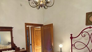 Ein Schlafzimmer mit einem Himmelbett, einer Holzkommode, einem Spiegel, einer Kandelaber und einer Tür zu einem anderen Raum.
