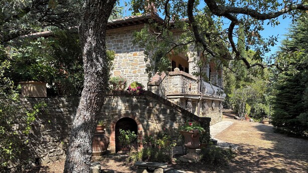 Ein Steinhaus mit einem steinernen Bogen, umgeben von Bäumen und Topfpflanzen.