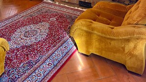Ein gemütliches Wohnzimmer mit Kamin, einem roten Blumensofa, einem senffarbenen Sessel und einem gemusterten Teppich.