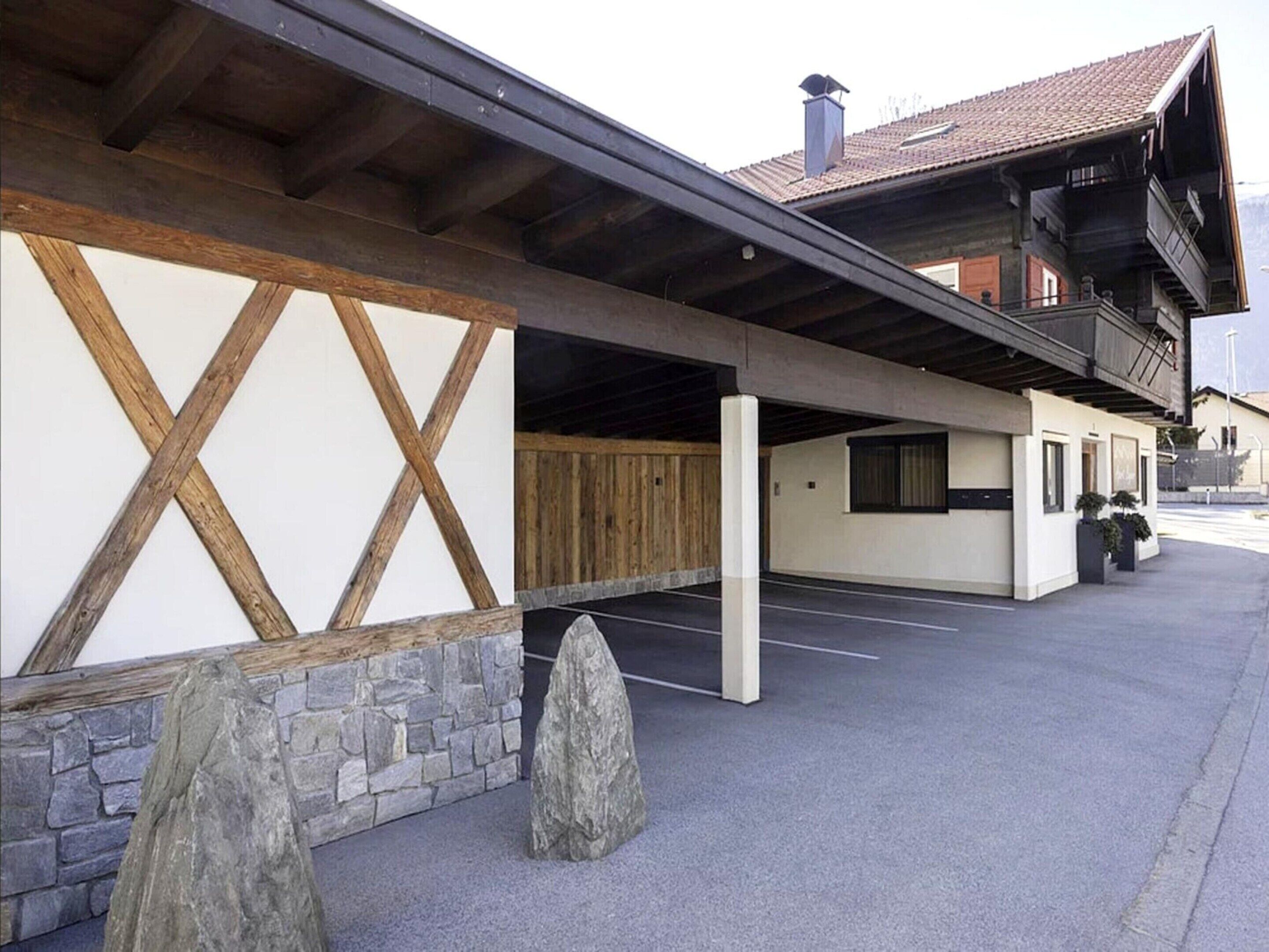 Ein Gebäude mit Natursteinfassade, Holzbalken und einem überdachten Parkbereich.