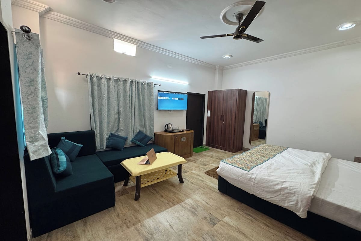A modern hotel room with a sofa, a bed, a small table, a wardrobe, and a ceiling fan.
