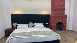 Une chambre avec un grand lit, deux lampes de chevet, une cheminée en briques et une table de chevet avec une lampe.
