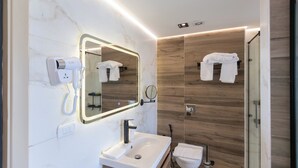 Un bagno moderno con un mobile vanitario in marmo, uno specchio grande, un asciugacapelli e pannelli in legno.