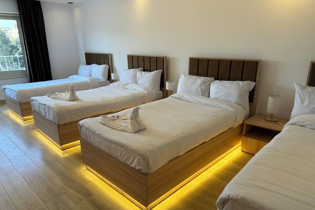 A hotel room with three beds, wooden headboards, white bedding, and bedside lamps.