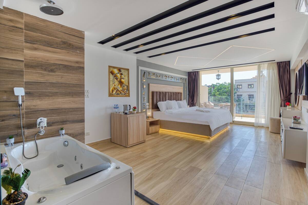 A modern bedroom with a large bed, a bathtub, and a balcony with a city view.