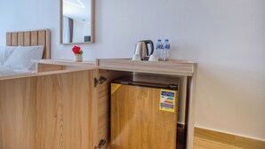 Una camera d'albergo con un letto di legno, un piccolo mobiletto in legno, un frigorifero, un bollitore e due bottiglie d'acqua.