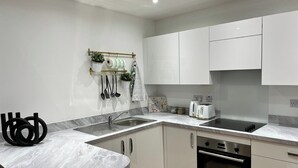 Une cuisine moderne avec des meubles blancs, un plan de travail en marbre, un évier, une bouilloire, un grille-pain et un four Samsung.