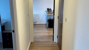 Un couloir étroit, doté d’un plancher en bois, mène à une pièce où se trouvent un lit et un radiateur.