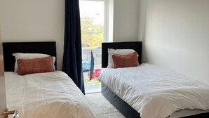 Une chambre d’hôtel avec deux lits simples, une grande fenêtre donnant sur la rue et une porte menant à l’extérieur.